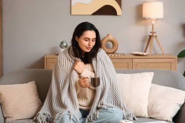 Evdeki kanepede oturan bir fincan sıcak çikolata ve ekoseli güzel, genç ve mutlu kadın.