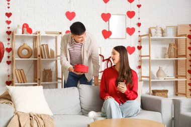 Young man greeting his beloved with gift at home on Valentine's Day