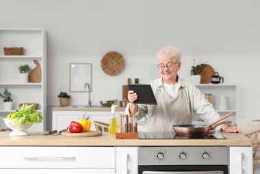 Mutfakta sebze kızartan tabletli son sınıf öğrencisi bir kadın.