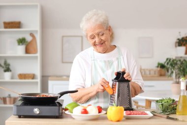 Mutfakta yemek pişirirken havuç rendeleyen son sınıf kadını.