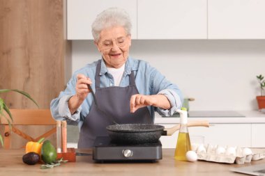 Kıdemli kadın mutfakta kızarmış yemek pişiriyor.