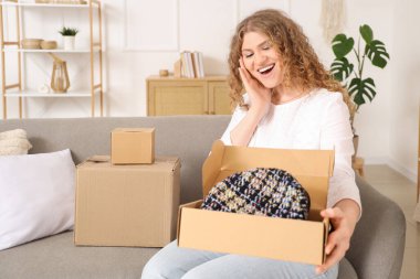 Evdeki kanepede yeni bereyle paket kutusunu açan genç bir kadın.