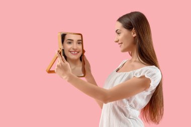 Genç bir kadın pembe arka planda aynaya bakıyor.