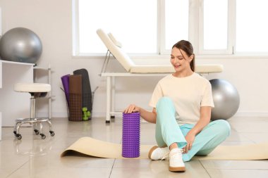 Rehabilitasyon merkezinde paspasın üzerinde köpük silindirli kadın fizyoterapist.
