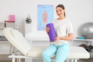 Rehabilitasyon merkezinde kanepede oturan köpük silindirli kadın fizyoterapist.