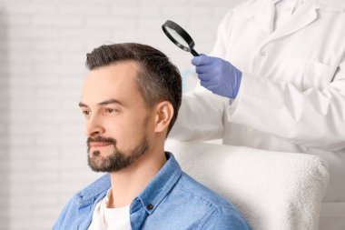 Büyüteçle trikoloğum klinikte adamın saçını inceliyor.