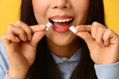 Güzel bir Asyalı kadın, ağzı açık, sarı arka planda sakız çiğniyor, yakın plan.