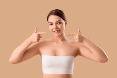 Gülümseyen genç bir kadın bej arka plandaki diş tellerine işaret ediyor.