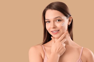 Diş teli takan genç bir kadın. Bej arka planda yüz kremi sürüyor. Yakın plan.