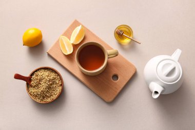 Bir fincan sıcak karabuğday çayı, limonlu ve ballı gri arka planda.