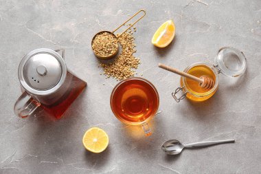 Cam bardak ve çaydanlık sıcak karabuğday çayı, limon ve bal kavanozu gri arka planda.