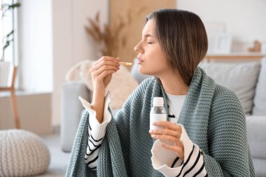 Ekoseli hasta genç kadın evde öksürük şurubu içiyor.