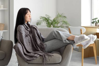 Gri ekoseli genç Asyalı kadın evdeki koltukta uzanıyor.