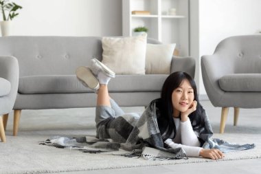 Evde yerde yatan yumuşak ekose kumaşlı genç Asyalı kadın.