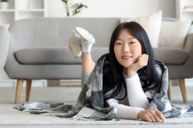 Evde yerde yatan yumuşak ekose kumaşlı genç Asyalı kadın.