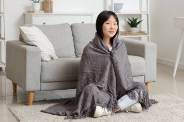 Gri battaniyeli genç Asyalı kadın evde yerde oturuyor.