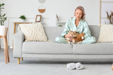 Pijamalı, yumuşak terlikli ve evdeki kanepede oturan güzel bir kadın.