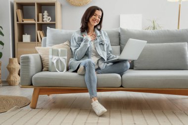 Hediye kutusu olan genç bir kadın evdeki kanepede internetten biriyle çıkıyor.