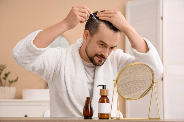 Красивый мужчина применяет сыворотку для роста волос в ванной комнате