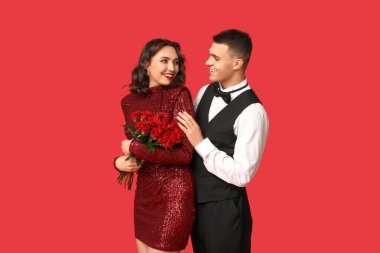Kırmızı arka planda sarmaş dolaş güzel güller taşıyan sevimli genç bir çift. Sevgililer Günü 'nün kutlaması