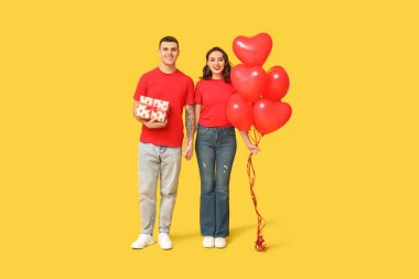 Kalp şeklinde balonları ve sarı arka planda hediye kutusu olan sevimli genç bir çift. Sevgililer Günü 'nün kutlaması