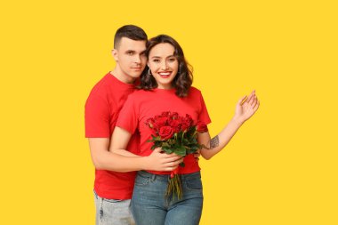 Sarı arka planda bir buket güzel gülleri olan sevimli genç bir çift. Sevgililer Günü 'nün kutlaması