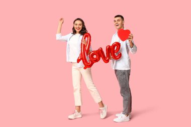 Aşk kelimesi şeklinde balonu ve pembe arka planda kağıt kalbi olan sevimli genç bir çift. Sevgililer Günü 'nün kutlaması