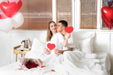 Güzel bir buket çiçekleri olan güzel bir çift yatak odasında yatıyor ve sevgililer gününü evde kutluyor.