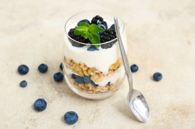 Hafif grunge arka planda yoğurtlu bir bardak lezzetli granola, yakın plan.