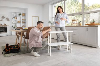 Mutlu hamile çift mutfaktaki raf ünitesini kuruyor.