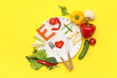 Tabak, çatal bıçak takımı ve VEGAN marka taze sebzelerden yapılmış renk arkaplanı.