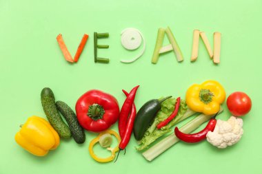 Yeşil arka planda VEGAN ve farklı sebzeler içeren kompozisyon