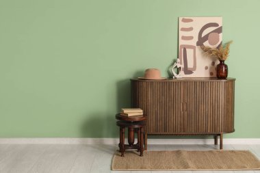 Çimen, resim ve kitaplarla dolu çekmeceler yeşil duvarın yanındaki taburede.