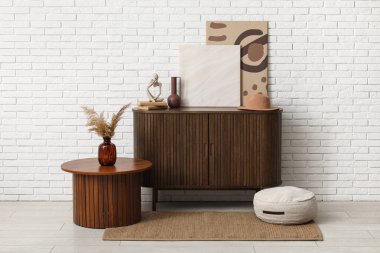 Çekmeceler, sehpa ve odadaki beyaz tuğla duvarın yanındaki resimler.