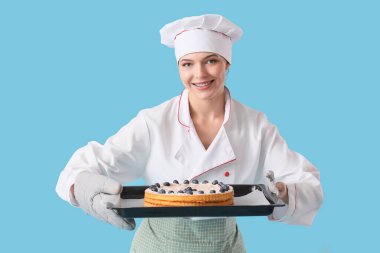 Kadın pastacı elinde kek tepsisiyle mavi arka planda