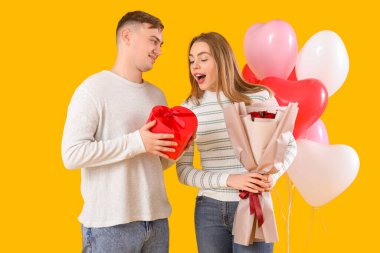 Hediye kutusu, çiçek buketi ve sarı arka planda kalp şeklinde balonları olan sevimli bir çift. Sevgililer Günü kutlaması