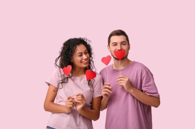 Pembe arka planda Sevgililer Günü için kağıt kalpli genç bir çift.