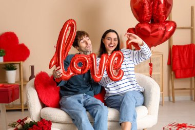 Young couple with air balloon in shape of word LOVE at home. Valentine's day celebration