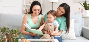 Evlatlık küçük kızı olan genç lezbiyen çift evde kitap okuyor.