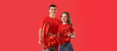 Kırmızı arka planda aşk kelimesi şeklinde balonları olan genç bir çift. Sevgililer Günü kutlaması