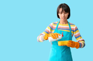 Mavi arka planda sünger ve deterjanı olan genç bir kadın.