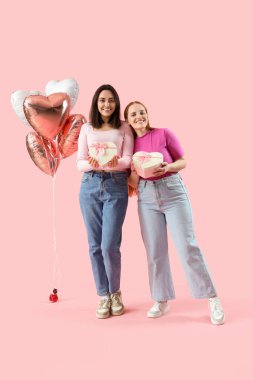 Pembe arka planda hediye kutuları ve balonları olan genç lezbiyen çift. Sevgililer Günü kutlaması