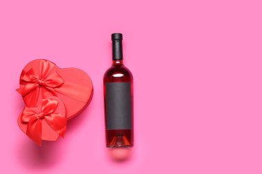 Pembe arka planda hediyeleri olan bir şişe şarap. Sevgililer Günü kutlaması