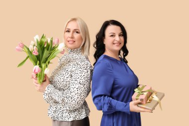 Güzel lalelerle dolu buketi ve bej arka planda hediye kutuları olan olgun kadınlar. Uluslararası Kadınlar Günü