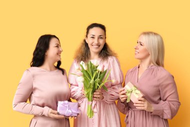 Güzel lalelerle dolu buketi ve sarı arka planda hediye kutuları olan olgun kadınlar. Uluslararası Kadınlar Günü