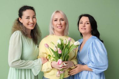 Yeşil arka planda bir buket güzel lalesi olan olgun kadınlar. Uluslararası Kadınlar Günü