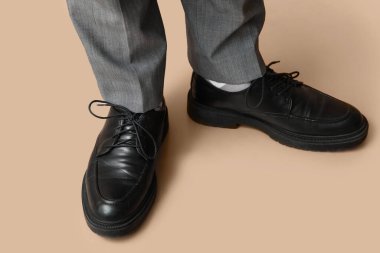 Kahverengi arka planda siyah şık ayakkabılı genç adamın bacakları.