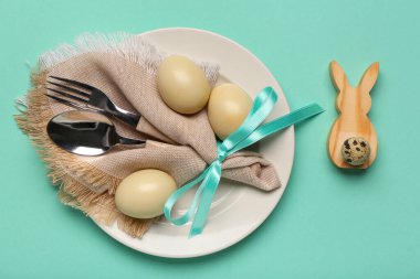 Paskalya yumurtaları, peçete ve turkuaz arka planda çatal bıçak seti olan şık bir masa.