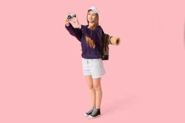 Gülümseyen genç bir kadın pembe arka planda fotoğraf çekiyor. Seyahat kavramı