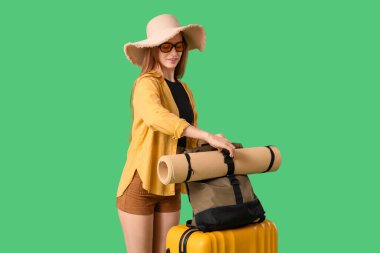 Şapkalı ve güneş gözlüklü gülümseyen genç kadın yeşil arka planda kamp paspası alıyor. Seyahat kavramı